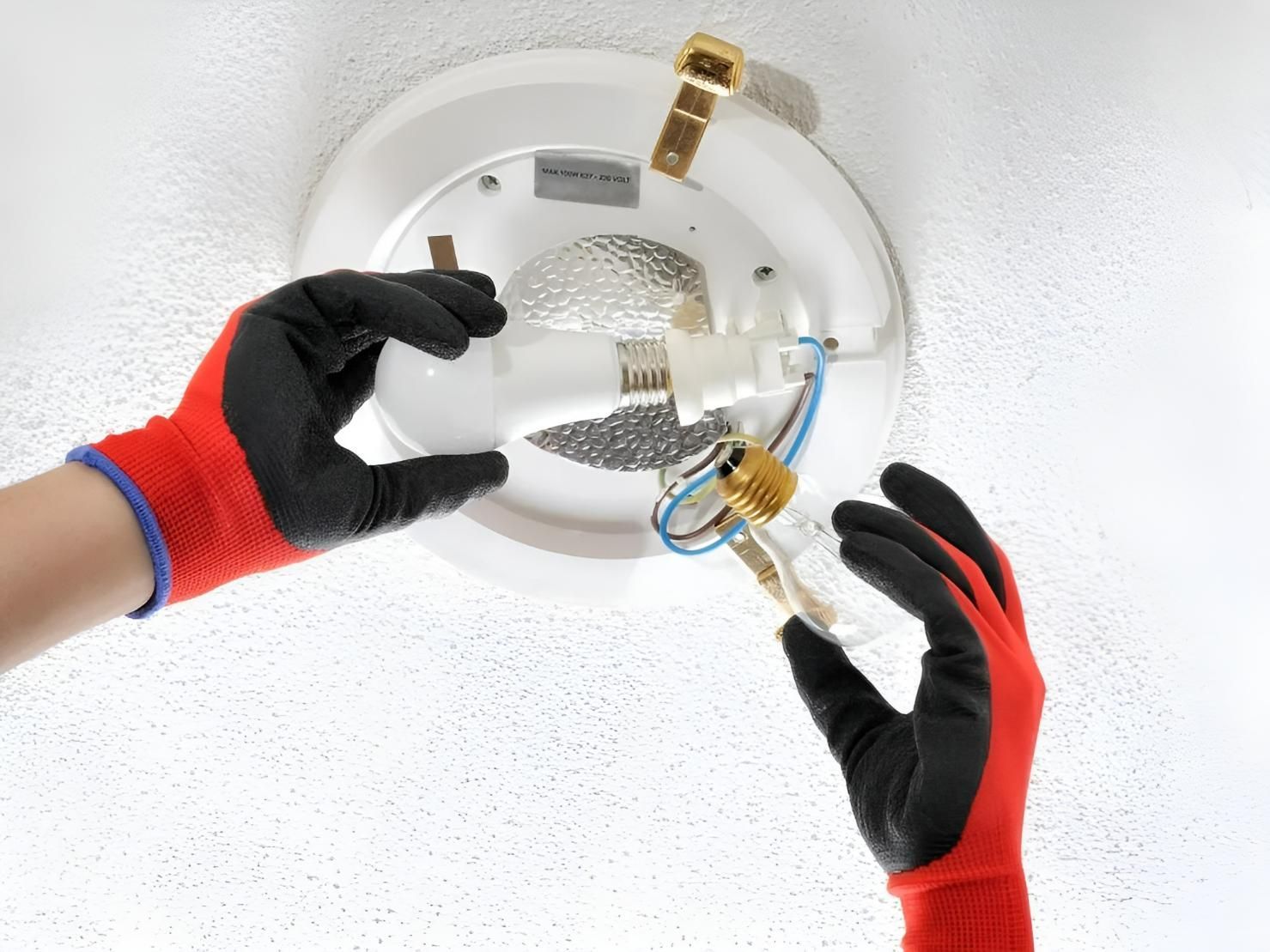 A Person Wearing Red Gloves is Installing a Light Bulb in a Ceiling — Clifford Electrical in Ballina, NSW