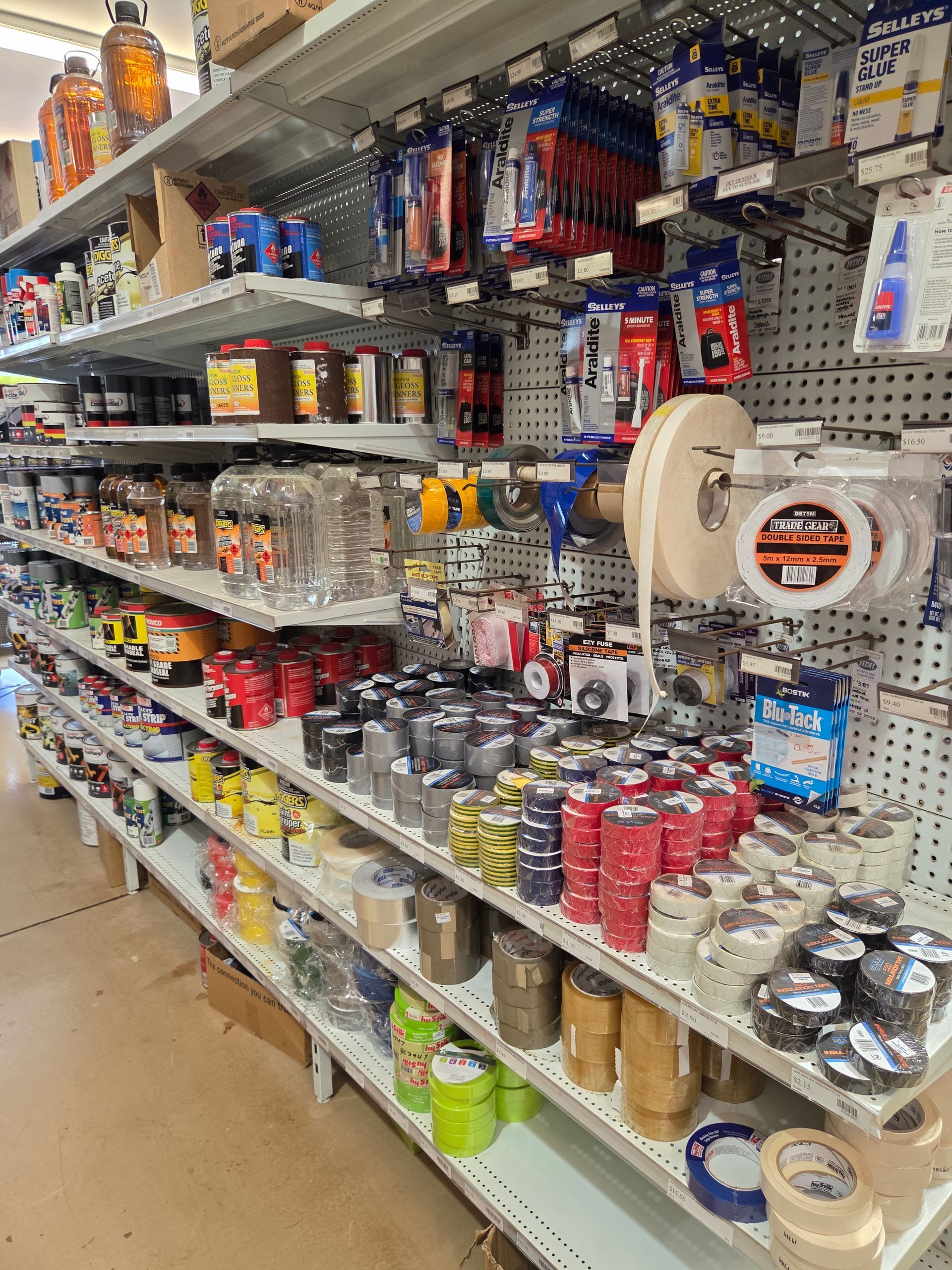 A store aisle stocked with hardware supplies, including tools, tape, batteries, and paint cans. — Humpty Doo Hardware in Humpty Doo, NT