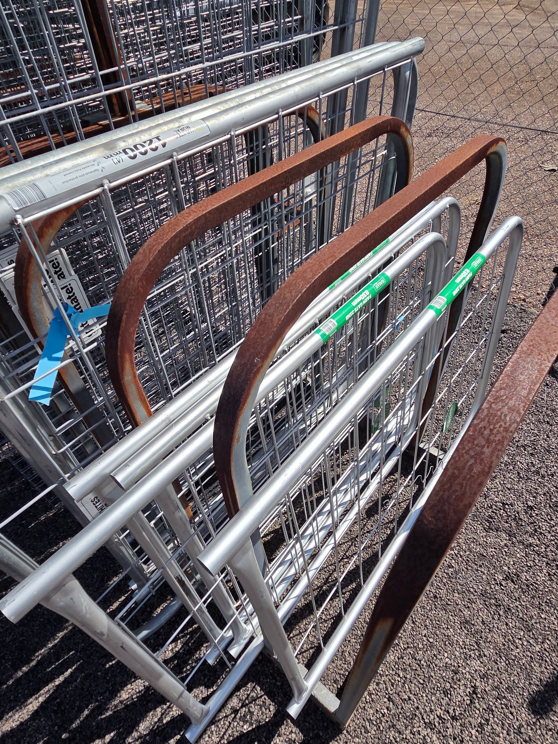 Stacked folding carts with metal frames and brown handles leaning against a wire fence on gravel. — Humpty Doo Hardware in Humpty Doo, NT