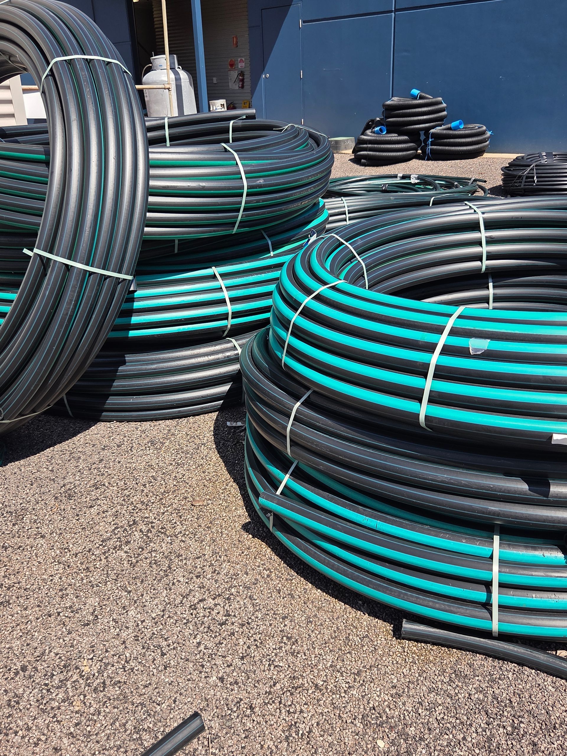 Coiled black and teal hoses stacked outdoors on gravel near industrial equipment — Humpty Doo Hardware in Humpty Doo, NT