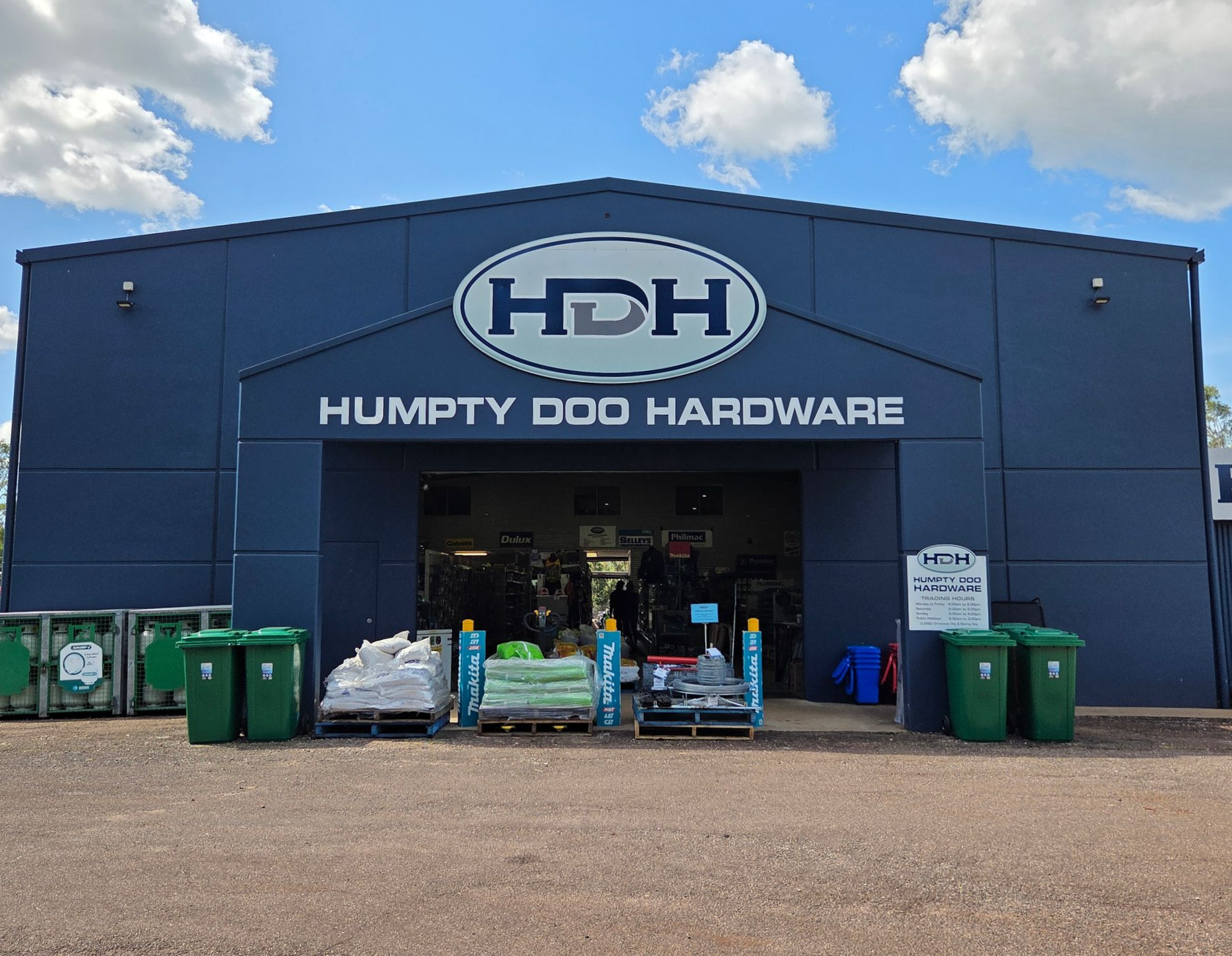 Humpty Doo Hardware storefront with blue facade, open entrance, and outdoor carts and bins under a cloudy sky — Humpty Doo Hardware in Humpty Doo, NT