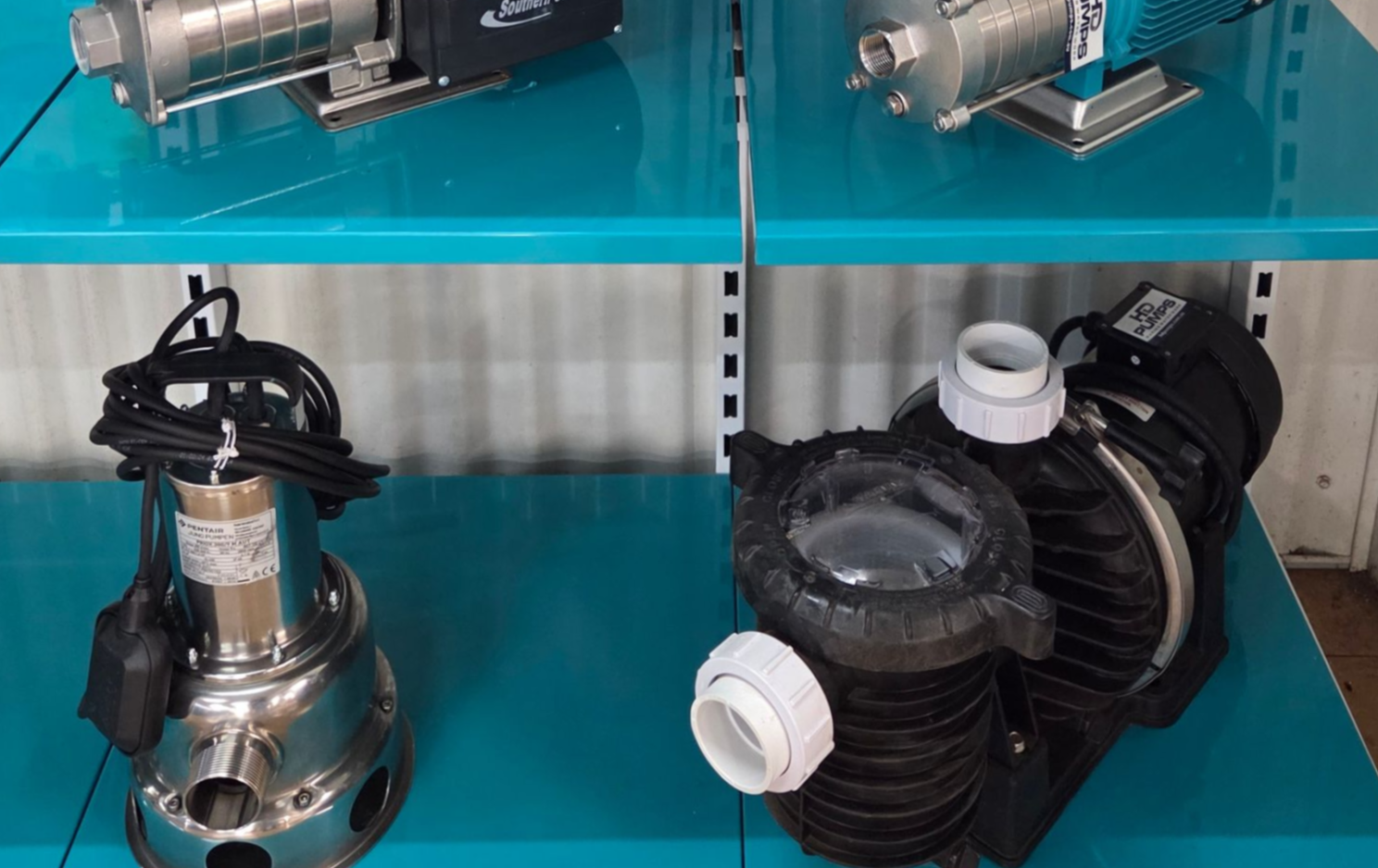 Industrial pumps displayed on turquoise shelves, including a shiny metal pump and a black pump with white fittings — Humpty Doo Hardware in Humpty Doo, NT