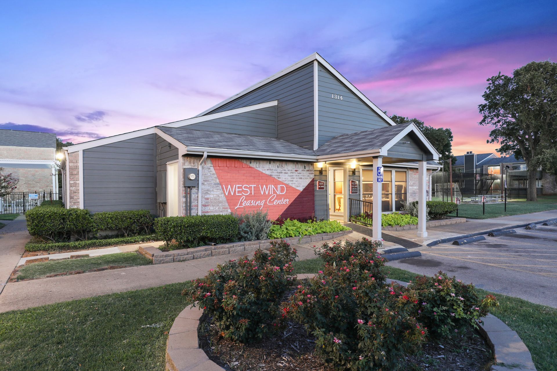 Apartment leasing office with red accent and purple sky. Bushes and walkway in front.