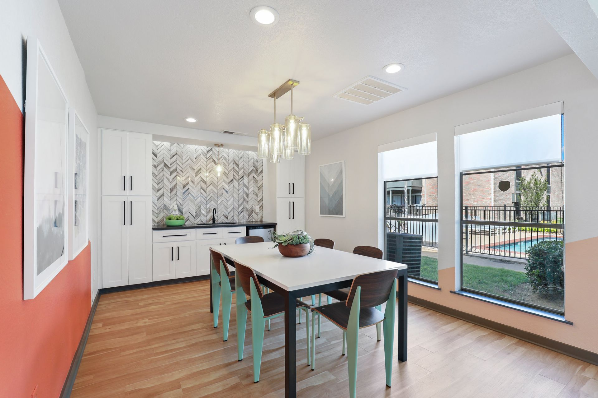 Dining area with a table, chairs, kitchen, and windows overlooking a pool.