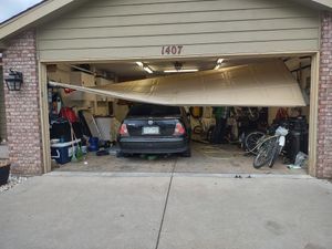 A residential garage door has come off its tracks and is hanging at an angle in front of a parked black sedan.