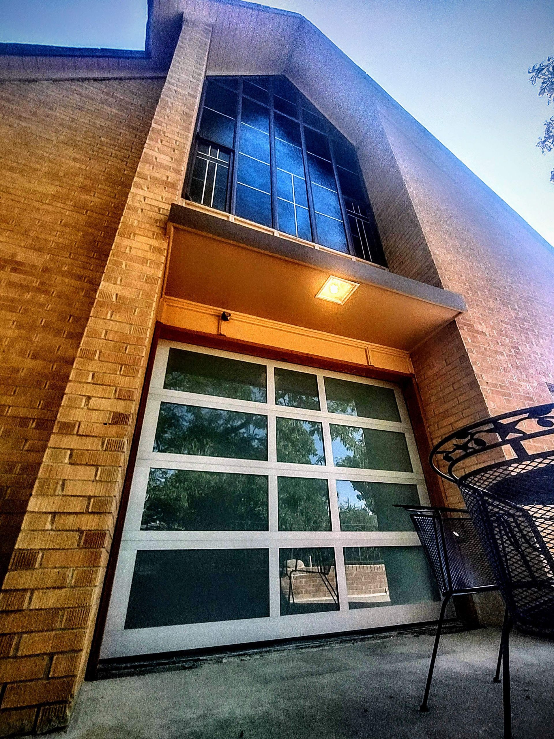 A low-angle view of a brick building featuring a large, multi-paned glass garage door and a tall, arched window above.