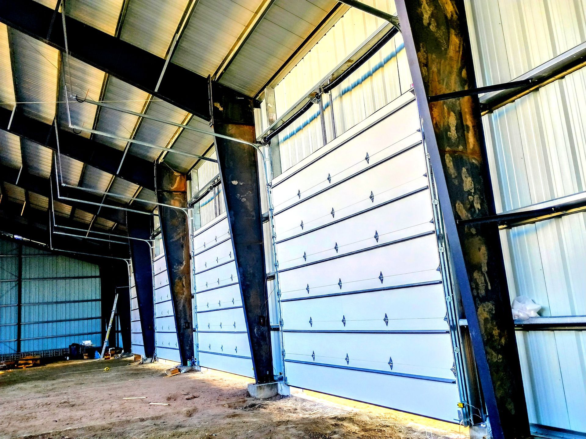 Interior view of a large metal building with a garage door installed between dark structural steel support beams.