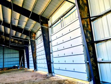 Interior view of a large metal building with a garage door installed between dark structural steel support beams.