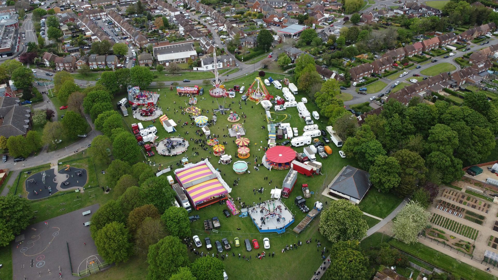 Aerial view of a funfair set up on a green park, surrounded by residential houses and trees.