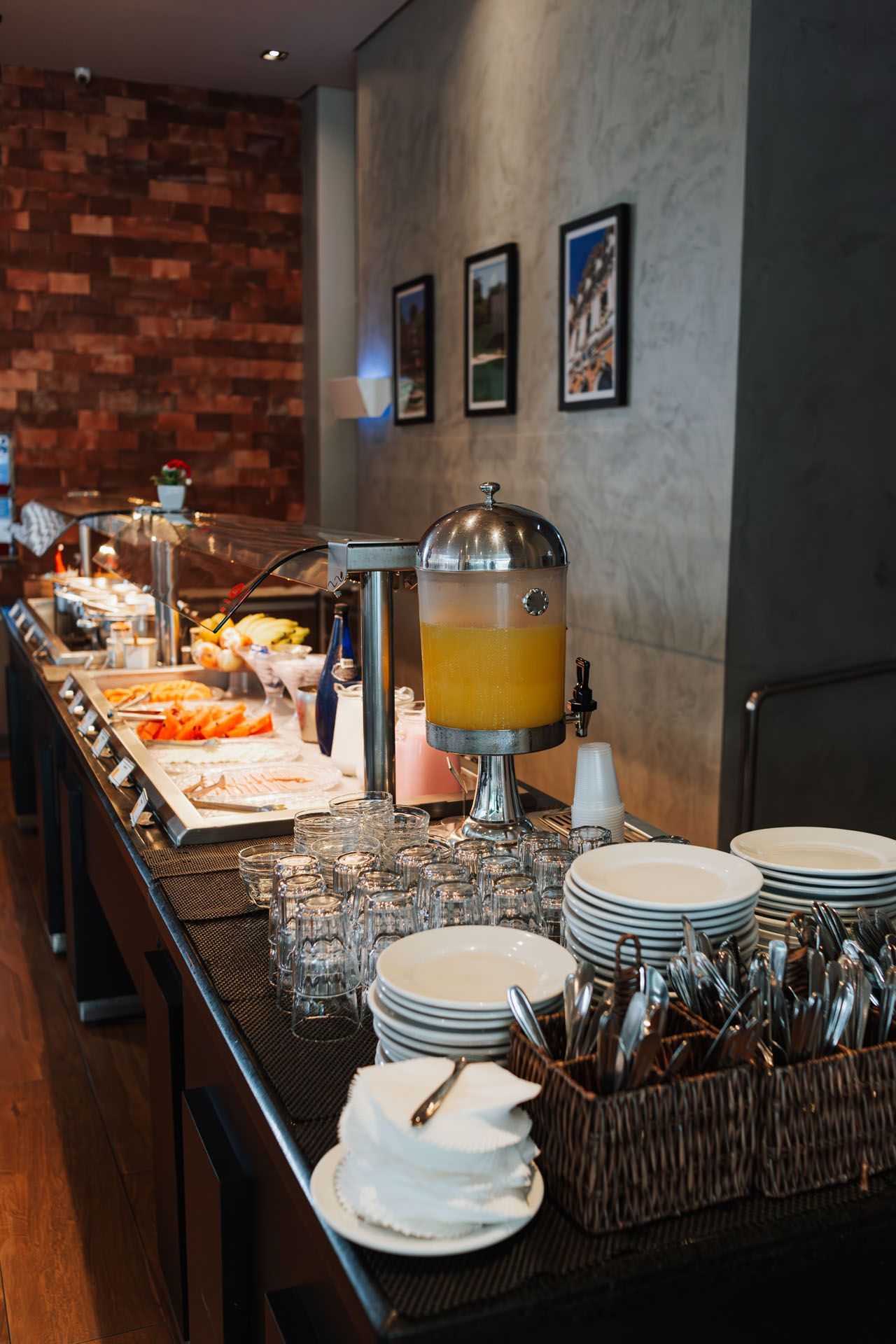 Mesa de buffet com bebidas, pratos e utensílios em uma área de jantar moderna.