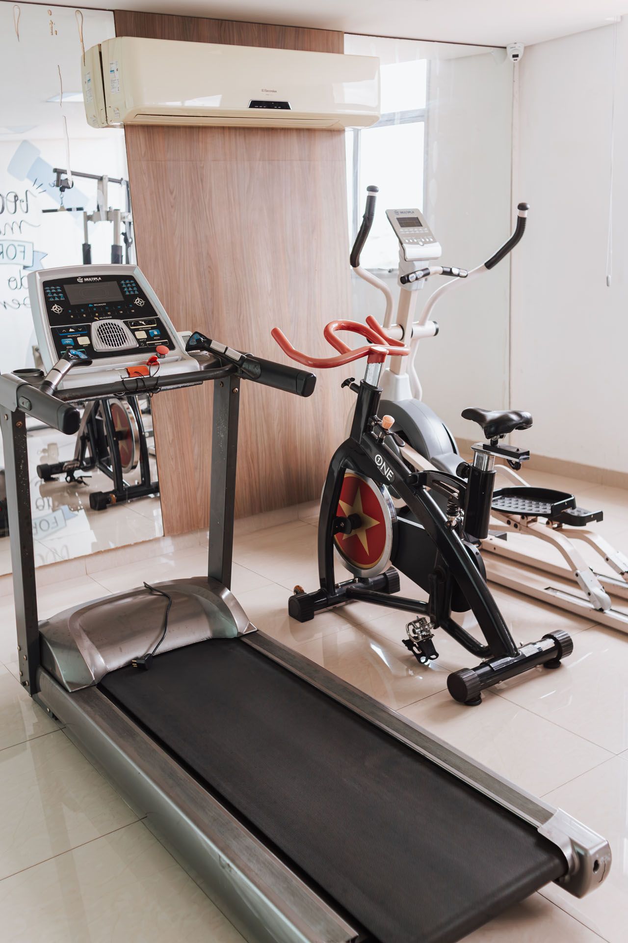 Academia em casa com esteira, bicicleta ergométrica e aparelhos de musculação em um cômodo pequeno.