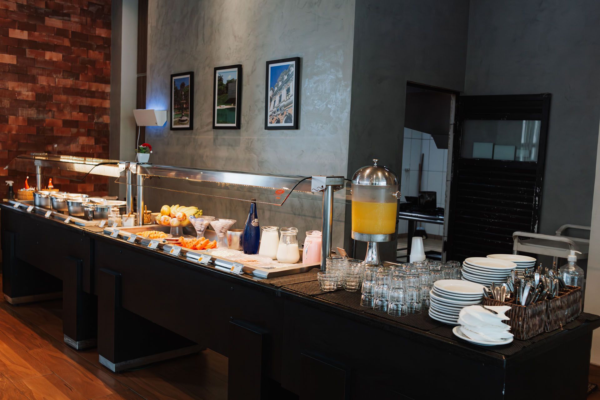 Mesa de buffet do hotel com doces, frutas, bebidas e pratos empilhados em uma área de refeições.