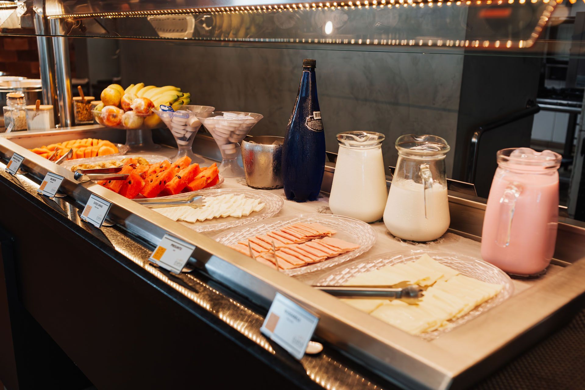 Buffet de café da manhã com frutas, doces e iogurte em potes de vidro em um balcão.