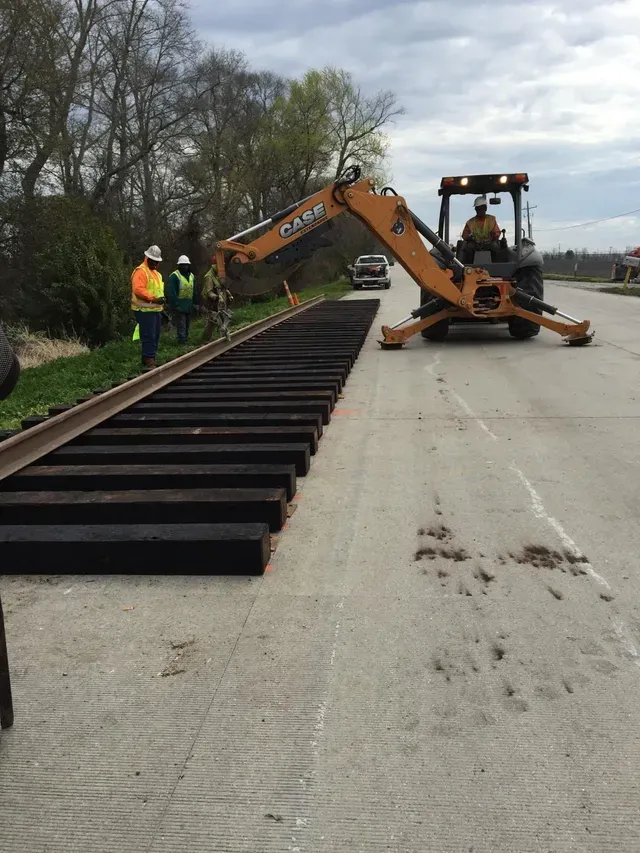 A tractor is moving train tracks on the side of a road.