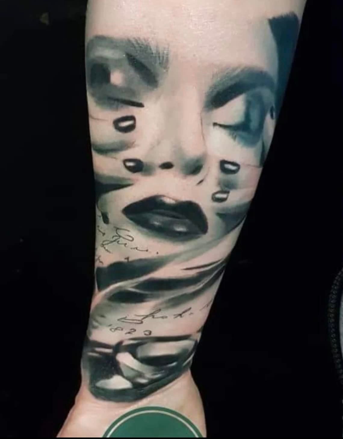 Een gedetailleerde zwart-grijze tatoeage op een arm, die een surrealistisch, gestileerd gezicht met vloeiende, abstracte lijnelementen toont.