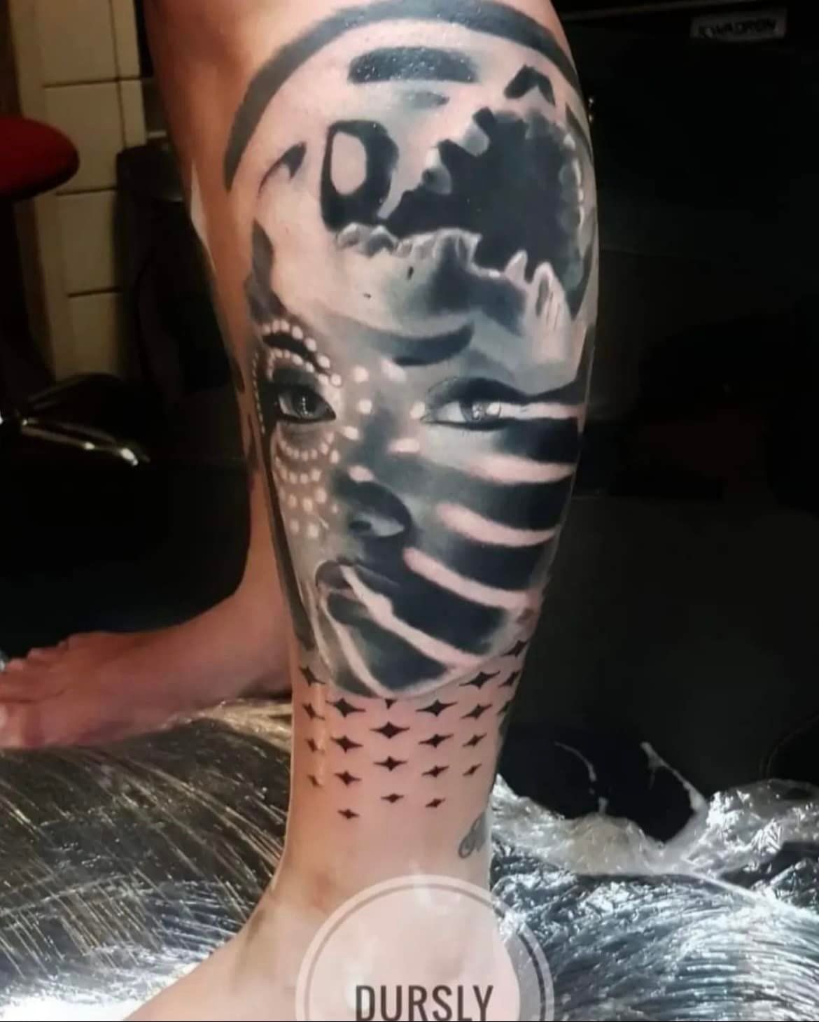 Een tatoeage op het onderbeen met een gezicht met een schaduweffect, stippen in tribale stijl en een geometrisch patroon als basis.