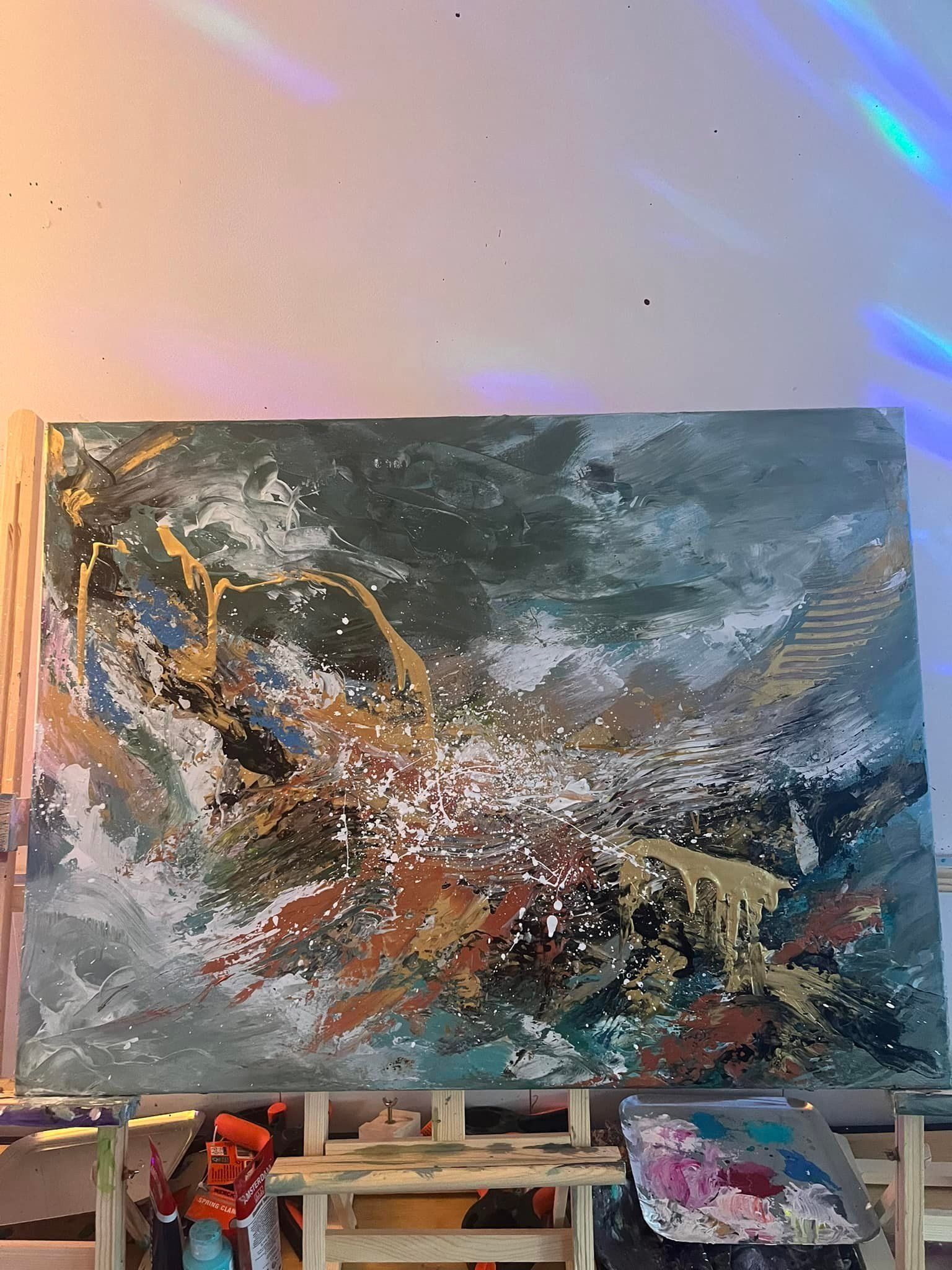Een abstract schilderij met gelaagde texturen in blauw, grijs en bruin, geaccentueerd met gouden druppels en witte verfspatten.