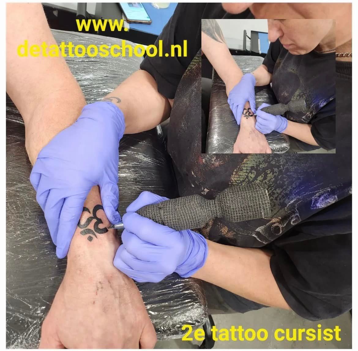 Een tatoeëerder met blauwe handschoenen tatoeert een Om-symbool op de pols van een persoon.