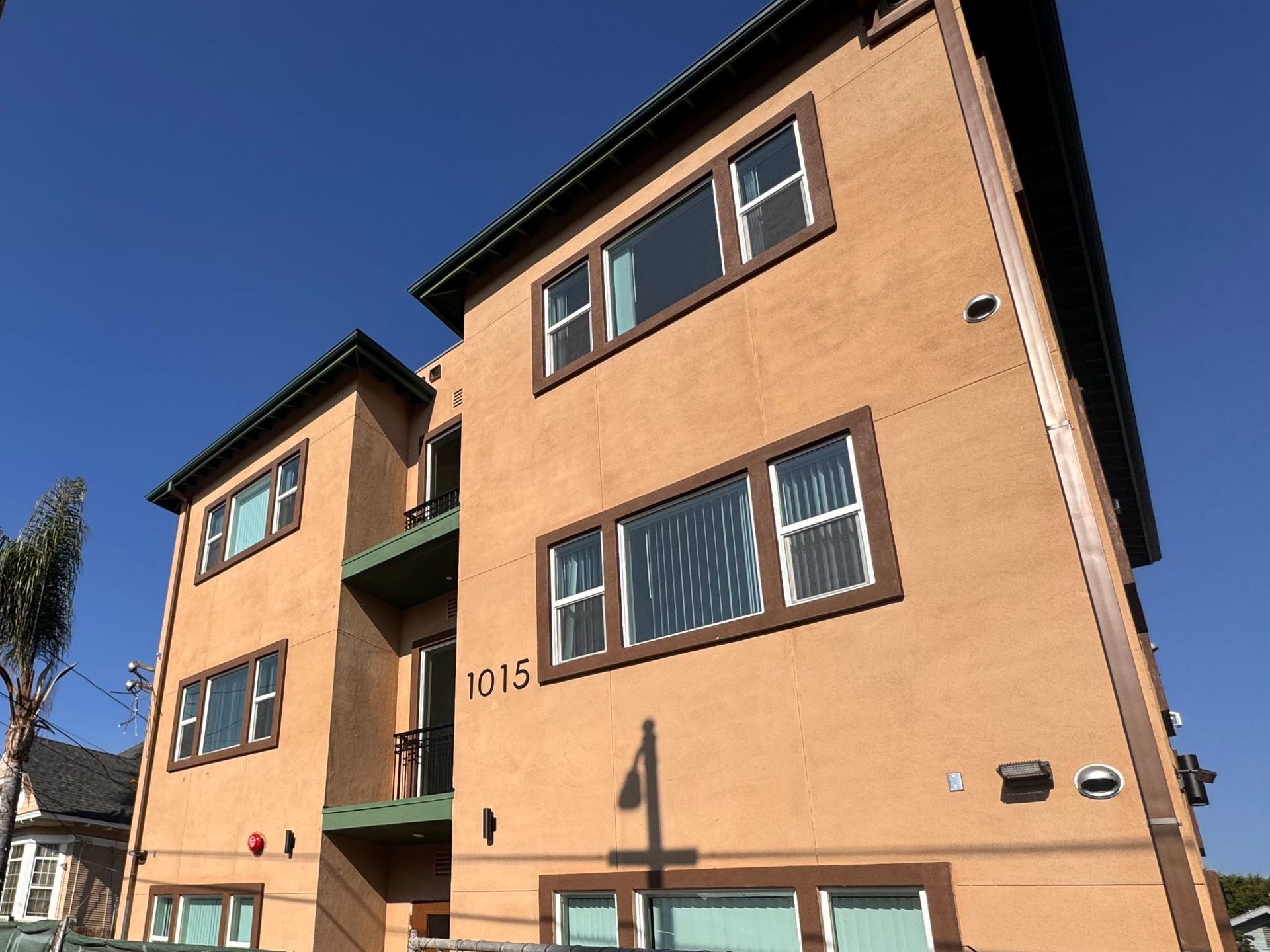 Three-story, beige apartment building numbered 1015, featuring brown-trimmed windows against a clear blue sky.