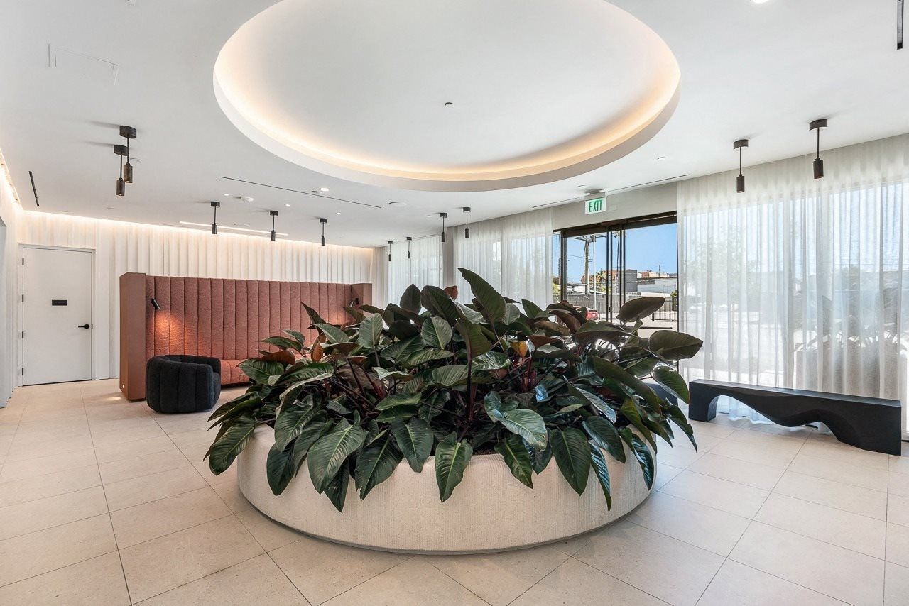 A bright lobby features a large central circular planter filled with lush green plants under a recessed ceiling light.