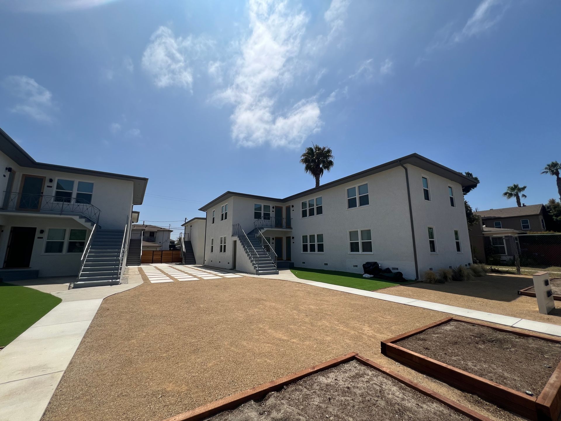 Two-story white apartment buildings surround a central courtyard with gravel, concrete paths, and raised garden beds.