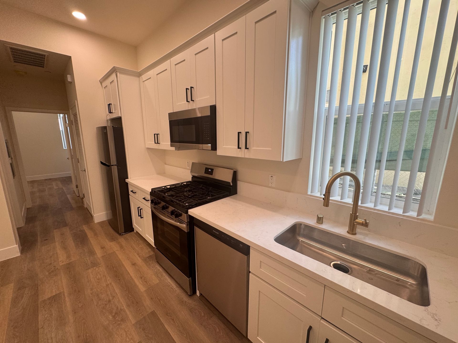 A modern kitchen with white cabinets, stainless steel appliances, a sink, and light wood-look flooring.