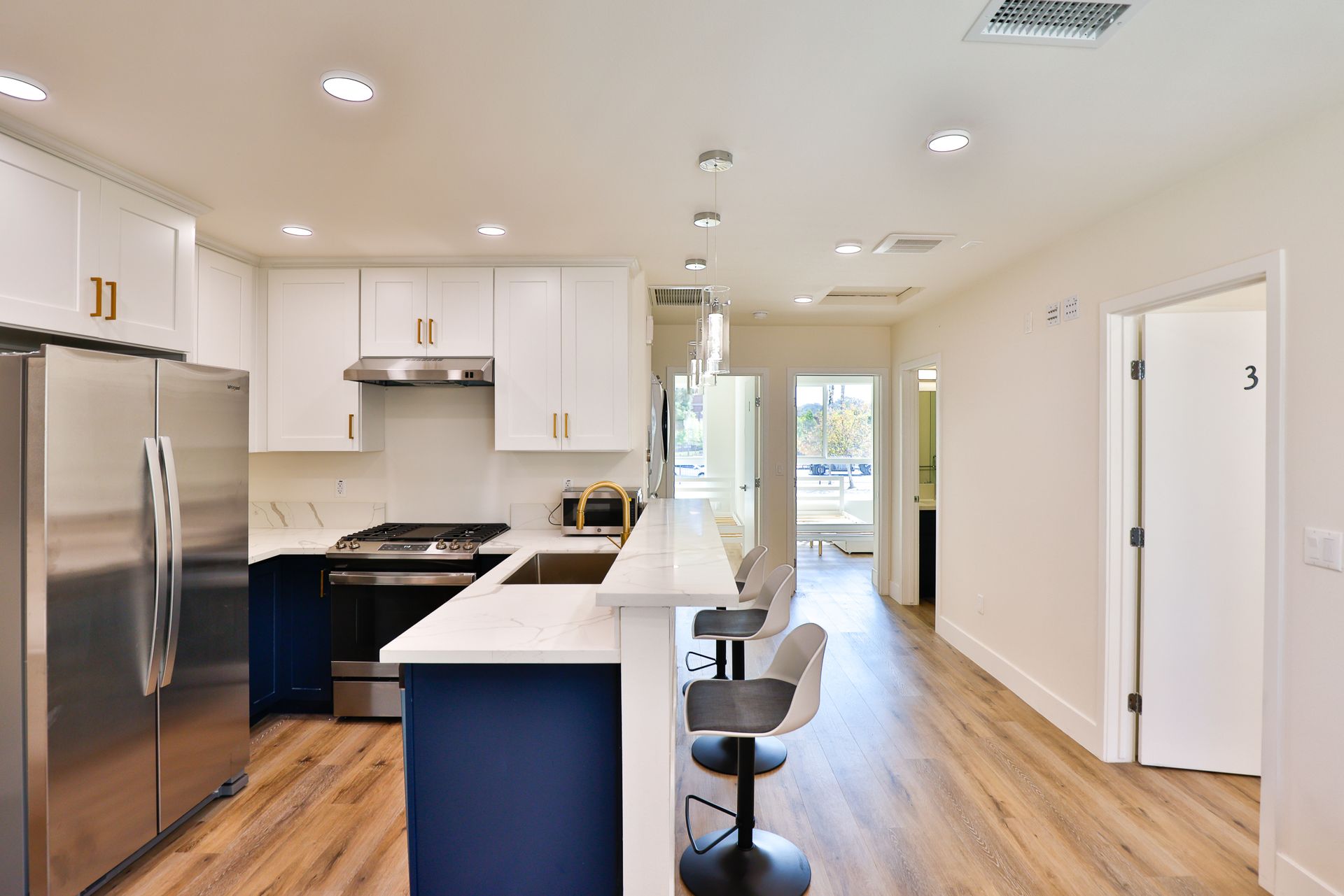 This image showing a white and blue theme kitchen room with a bar and stools.