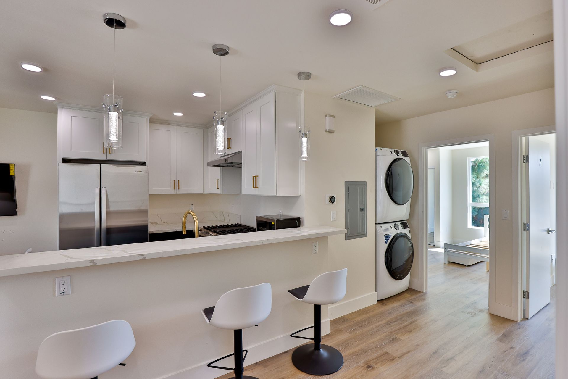 This image shows a white theme kitchen with white cabinets and appliances and the doors for the kitchen room are opened.