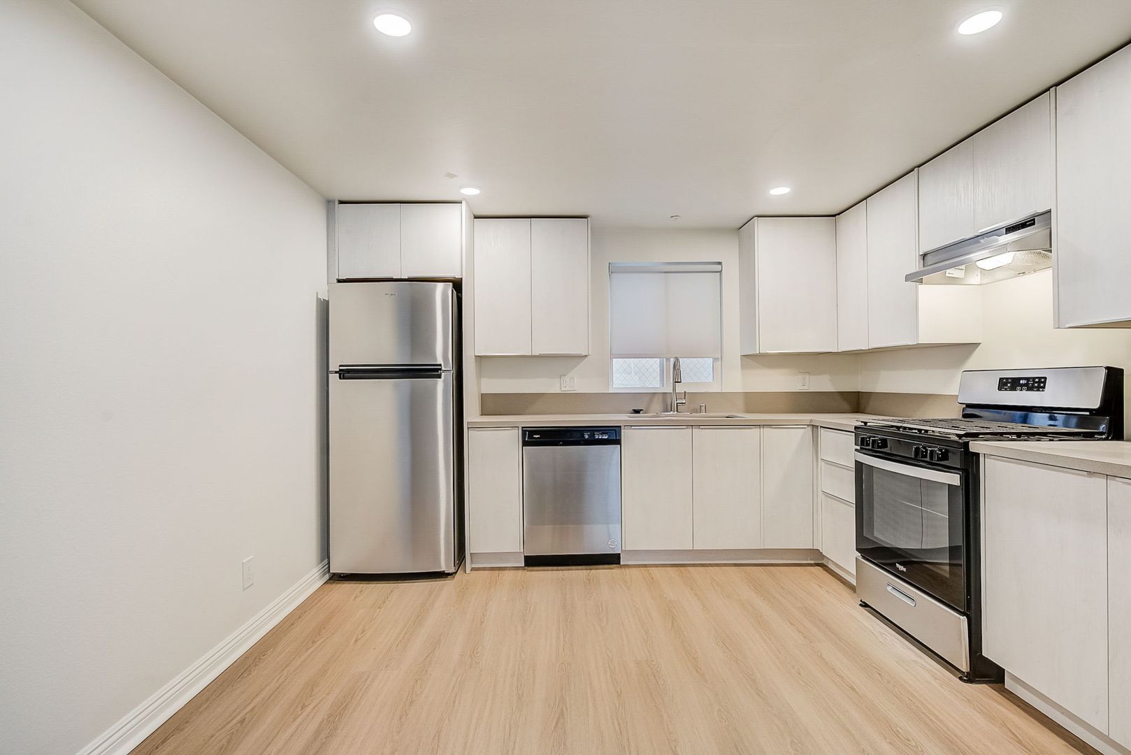 A bright kitchen with white cabinets, stainless steel appliances, and light wood-tone flooring.