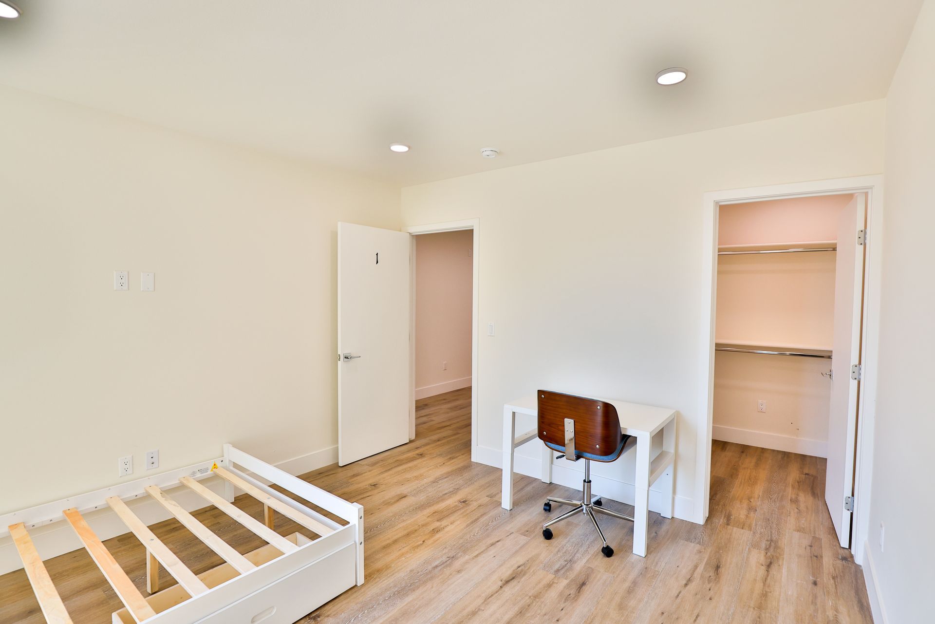 This image shows a room with a desk , brown chair and bed.