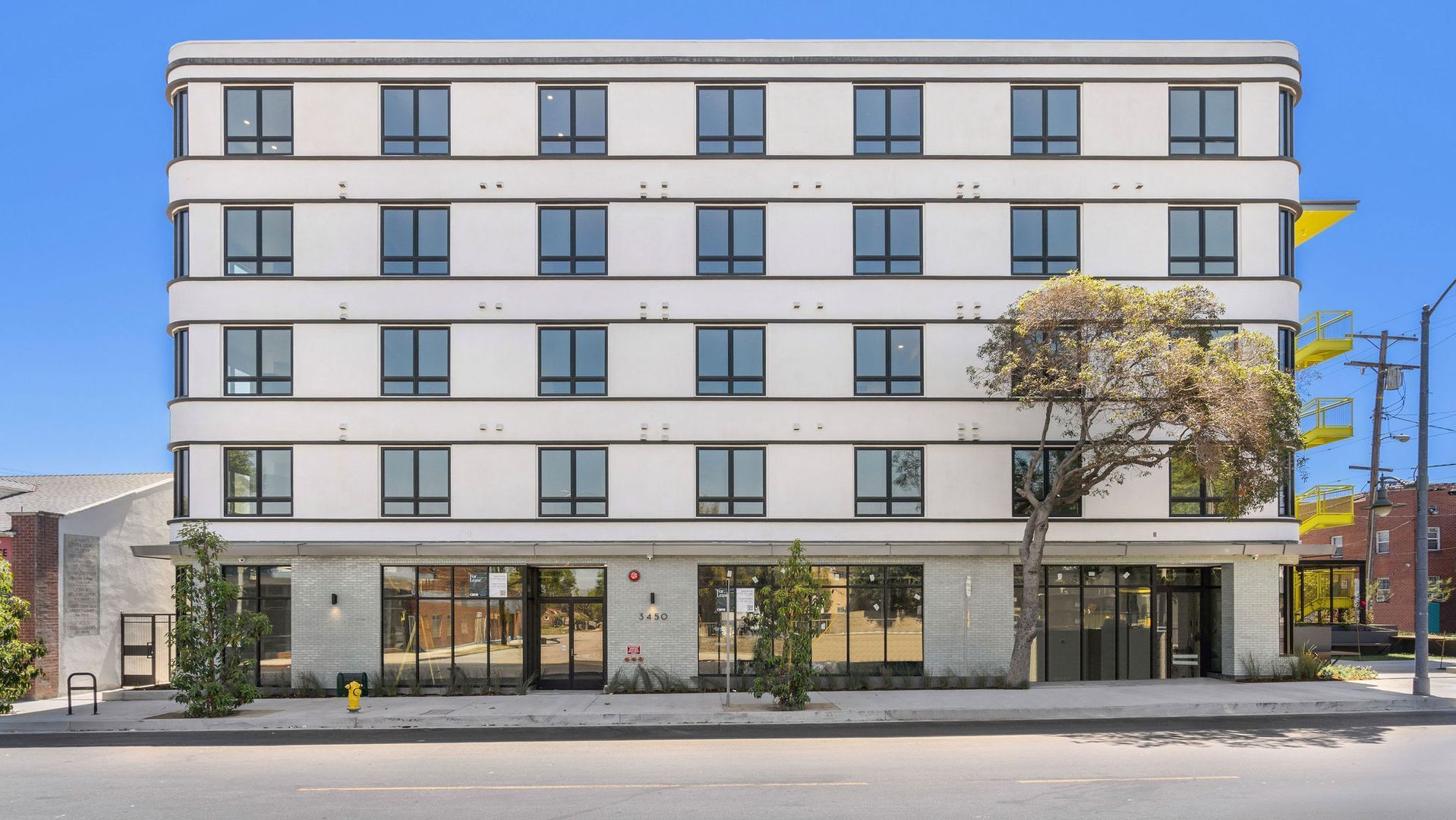 A four-story white building with a stone-textured ground floor and large windows under a clear blue sky.
