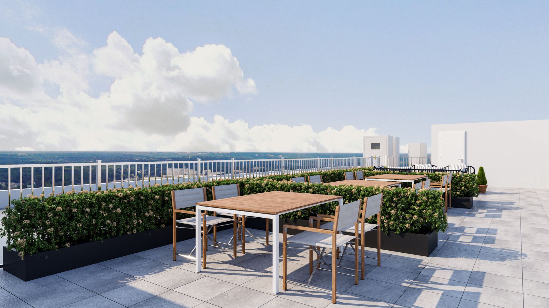 A modern rooftop terrace with outdoor dining tables and chairs surrounded by green hedges against a blue sky.