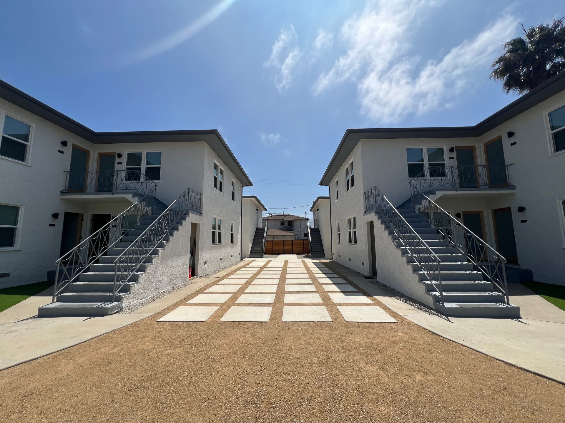 Two white, two-story apartment buildings face each other with exterior staircases and a gravel courtyard in between.