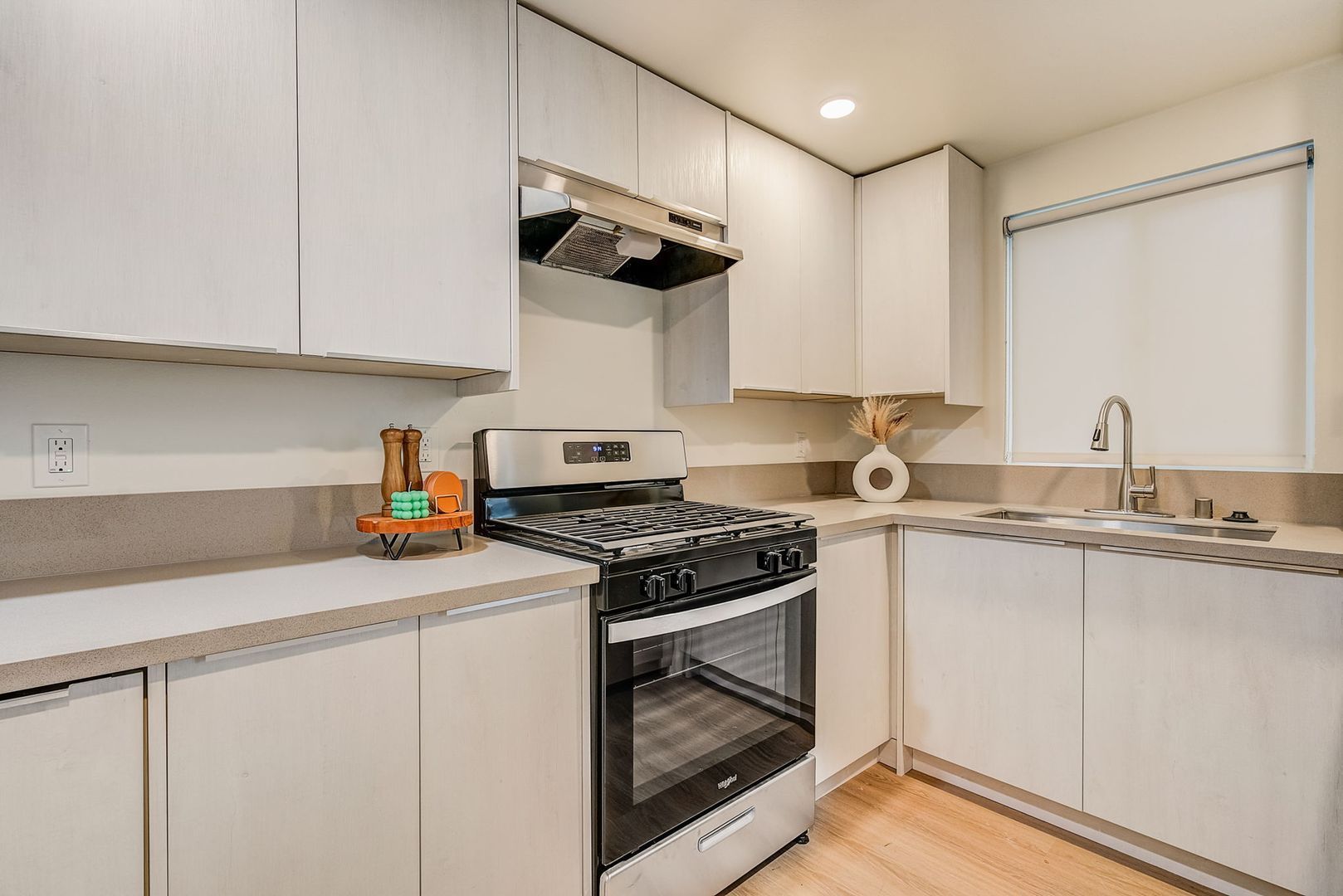 A kitchen with light-colored cabinets, a stainless steel gas stove, and a window above the sink.