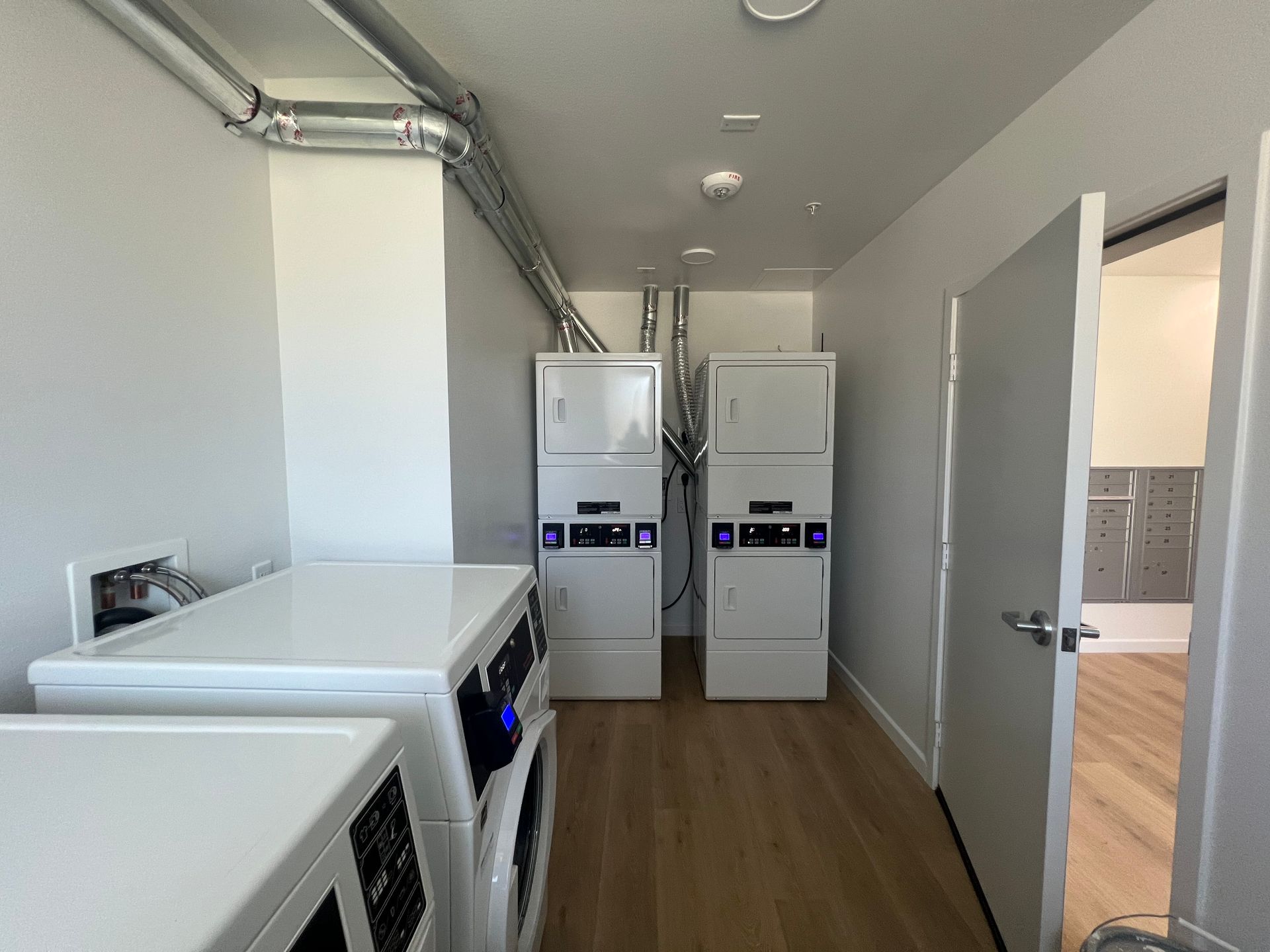 Laundry room with two stackable washing machines and dryers side-by-side, plus a partially visible unit in the foreground.