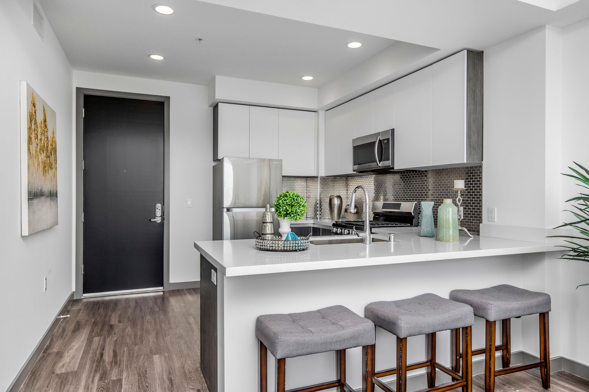 A modern kitchen with white cabinets, stainless steel appliances, a white quartz breakfast bar, and three gray stools.
