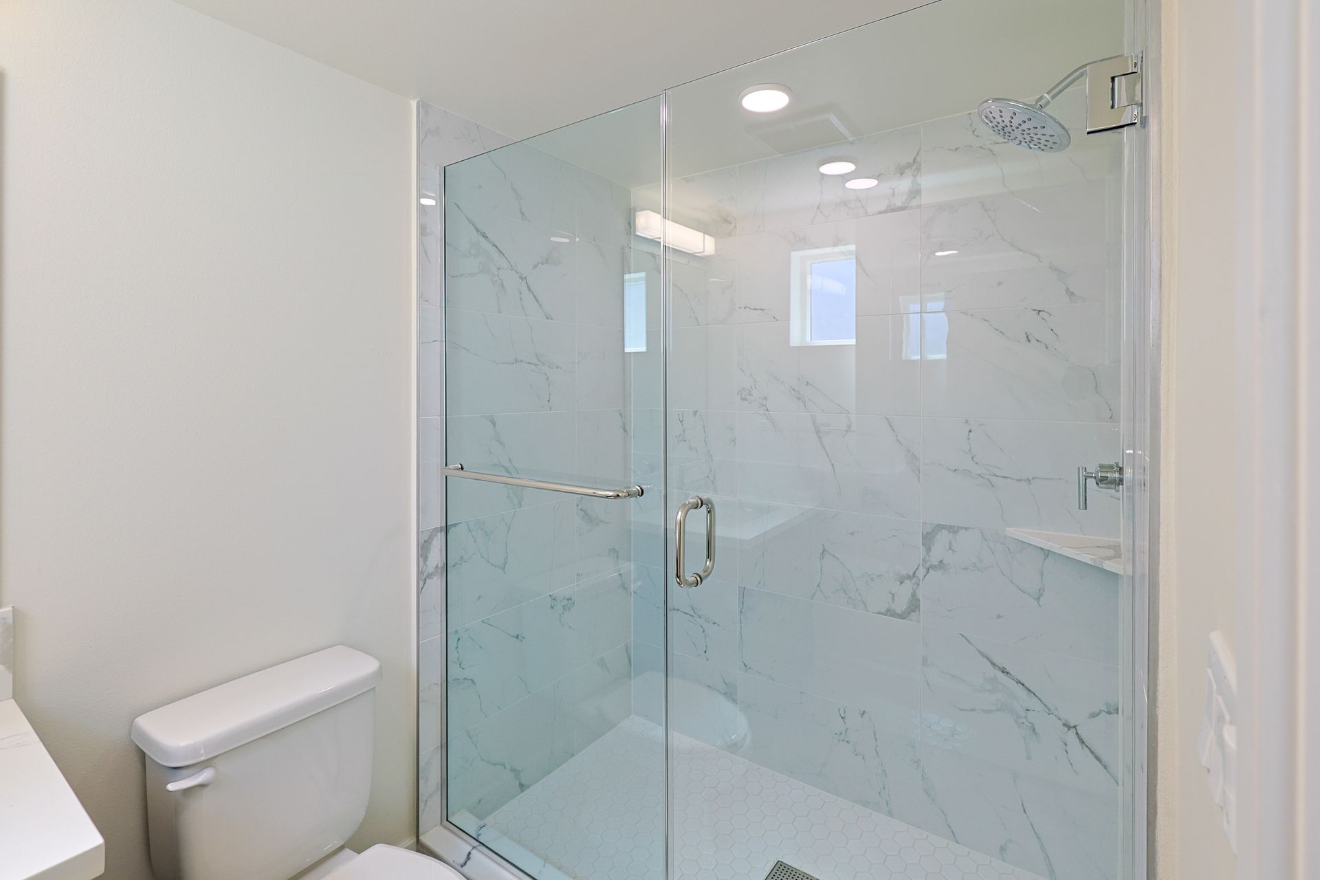 This image shows a bathroom with a glass shower and toilet having white walls .