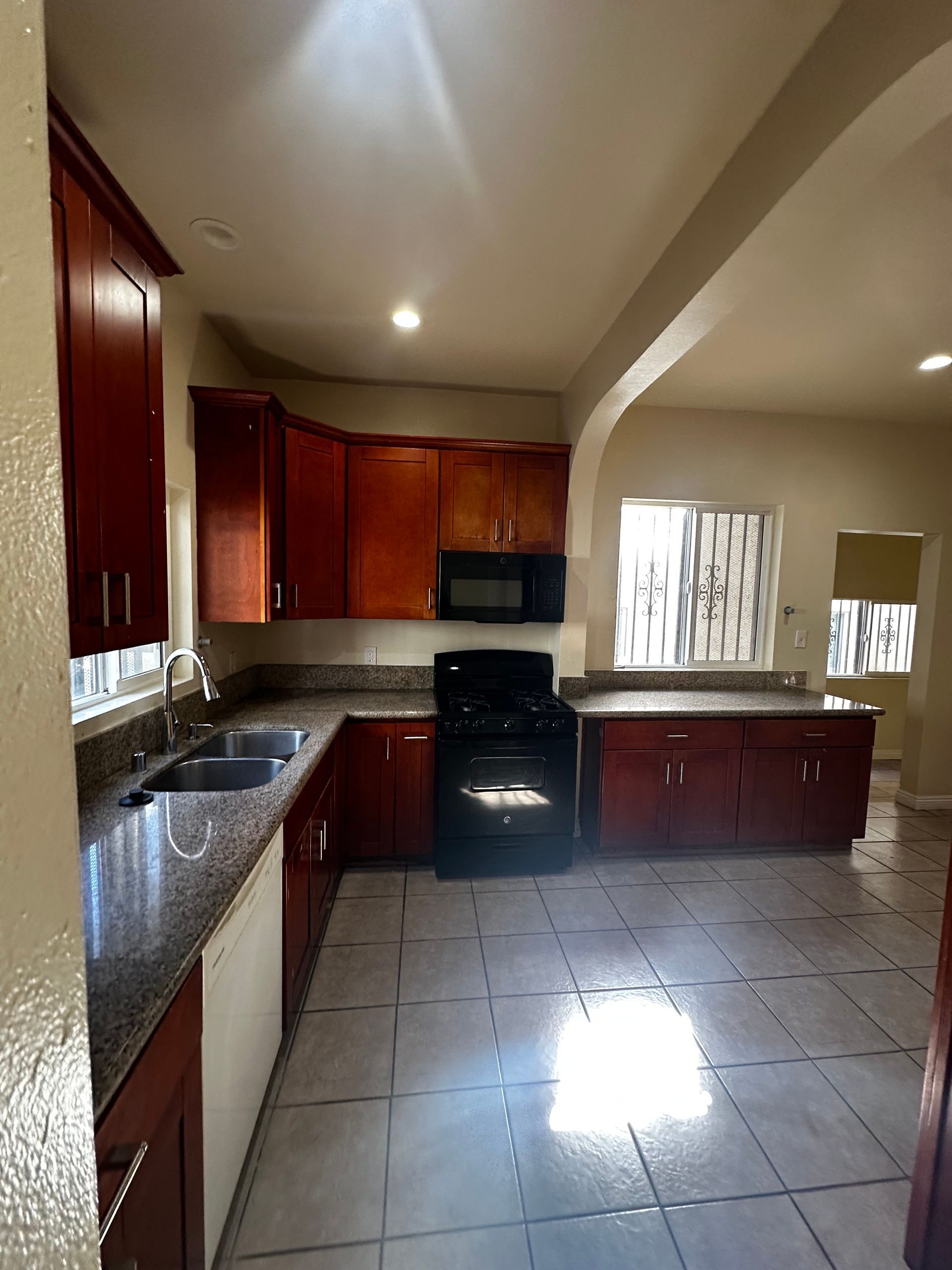 Kitchen with cherry wood cabinets, granite countertops, a black stove and microwave, and tiled floors.