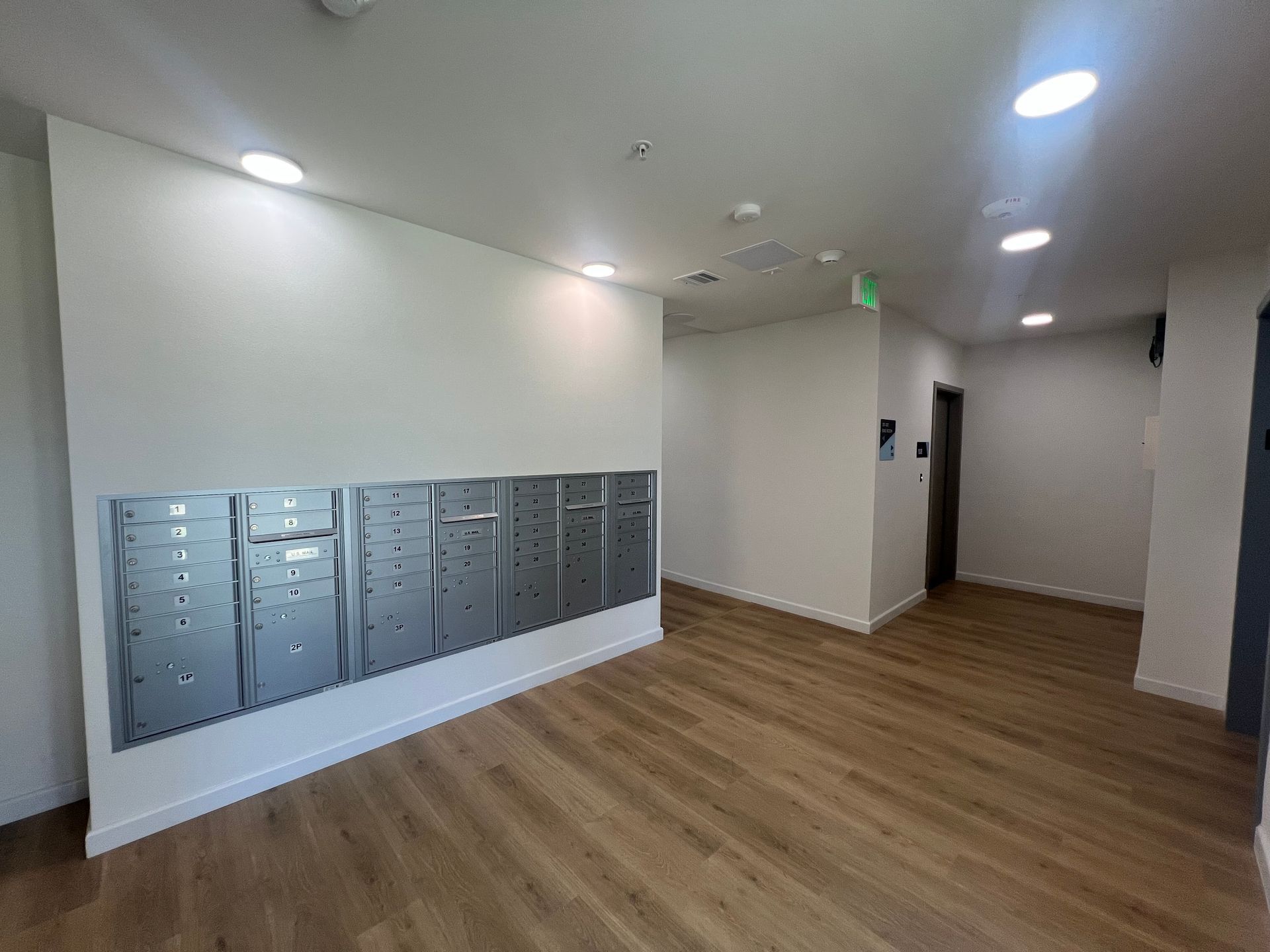 A wall of metal mailboxes in a brightly lit, modern apartment building lobby with wood-style flooring.