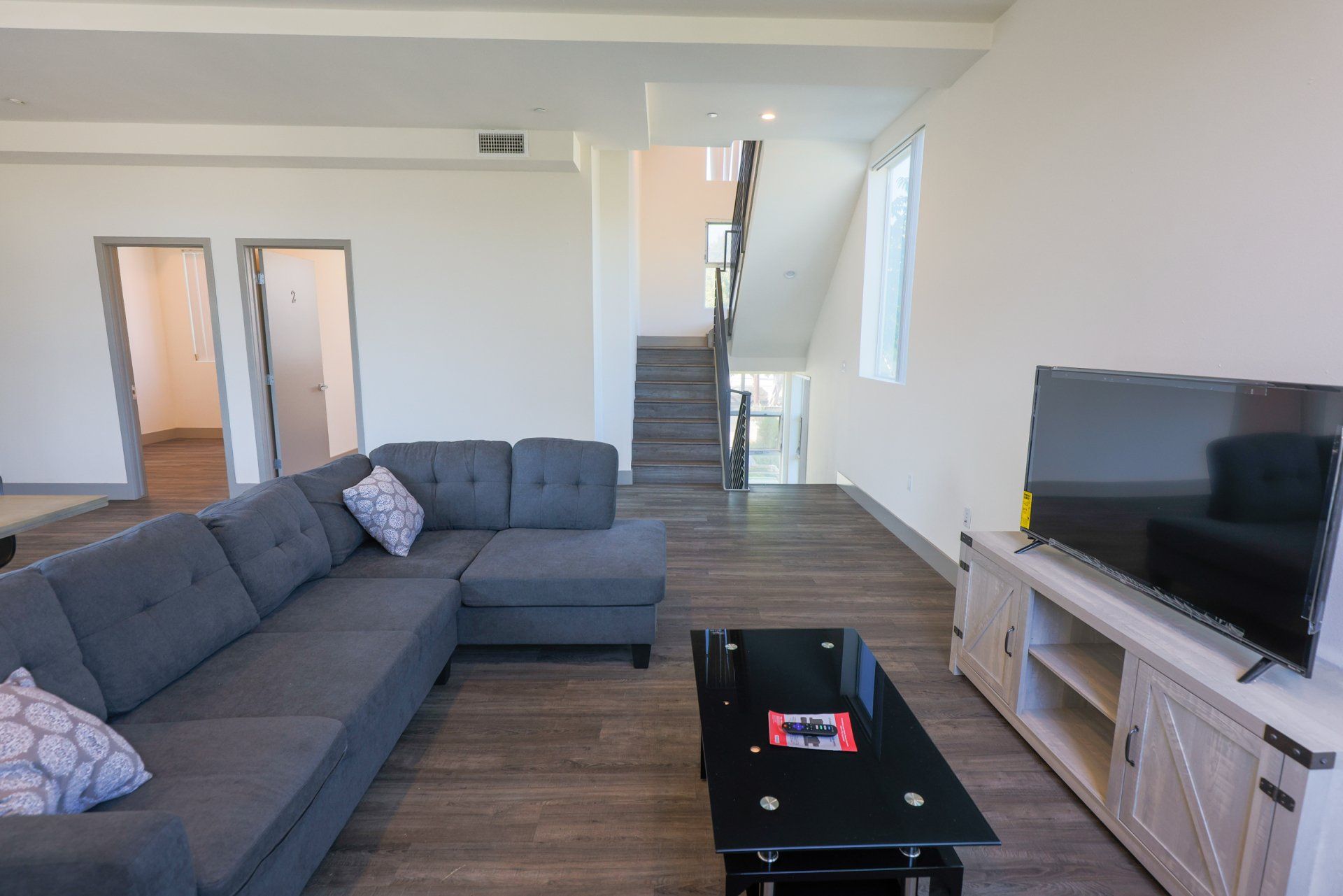 this image is showing a living with smart tv, coughs , two rooms and stairs in it.