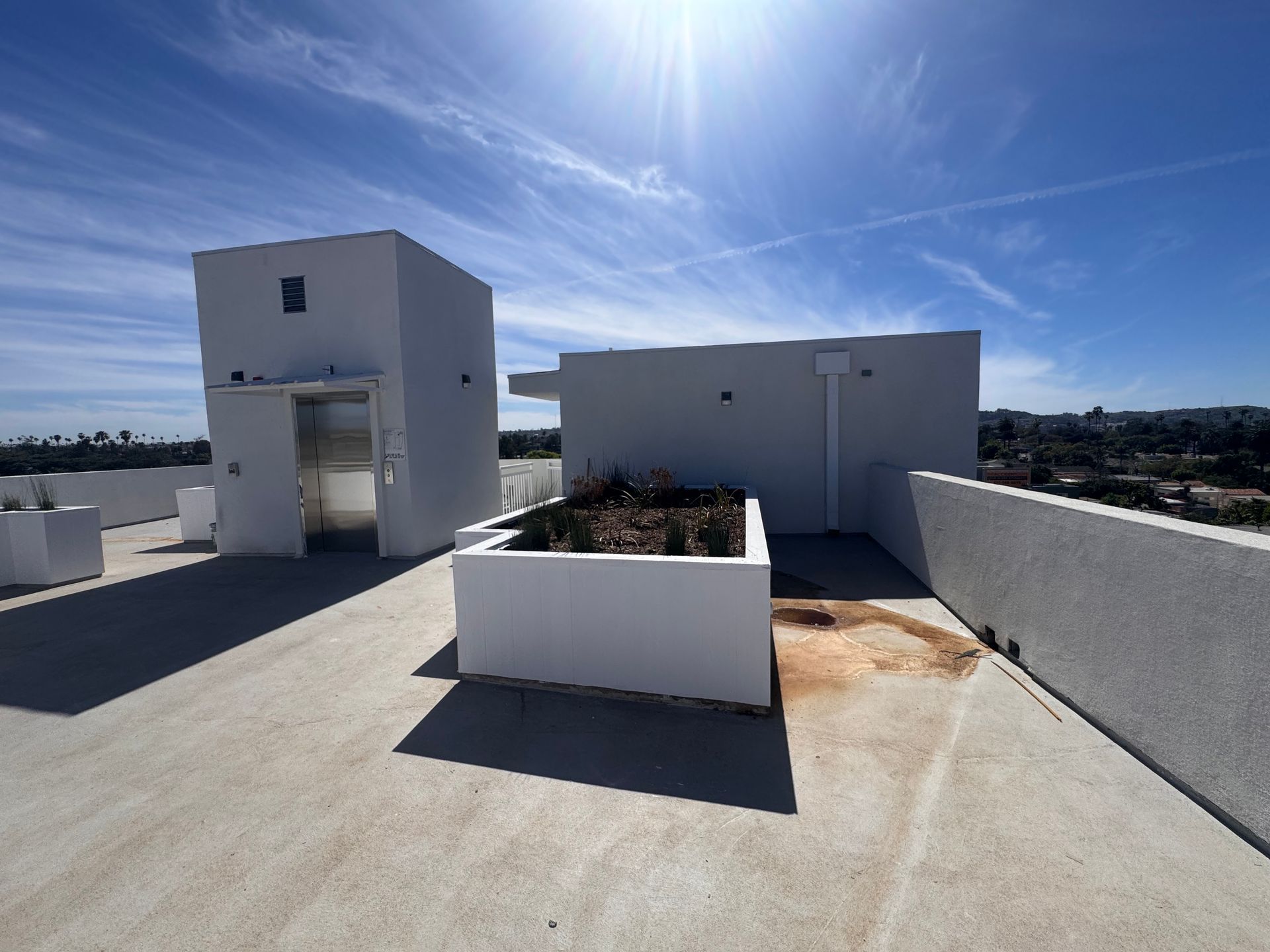 A white rooftop structure with a planter box and elevator entrance under a bright blue sky.