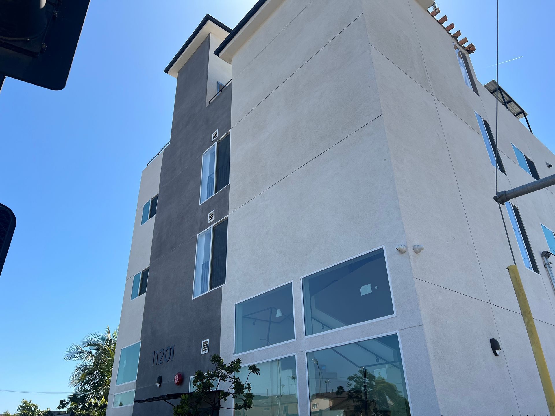 A modern three-story building with a light-colored stucco facade, a dark gray accent section, and large glass windows.