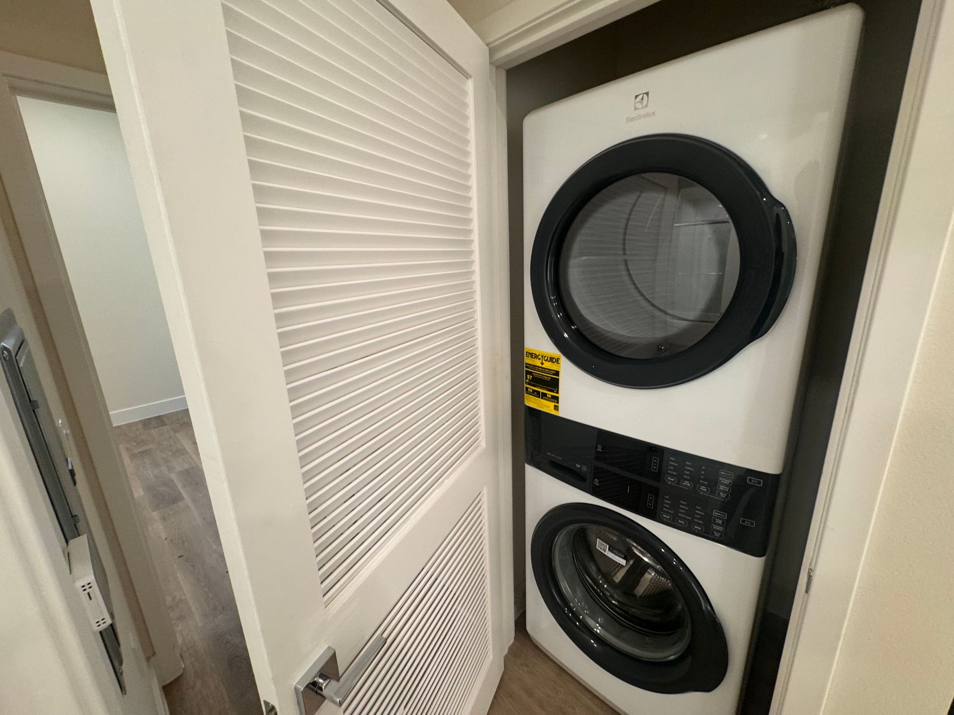 A white stacked washer and dryer unit housed in a small closet with a white louvered door.