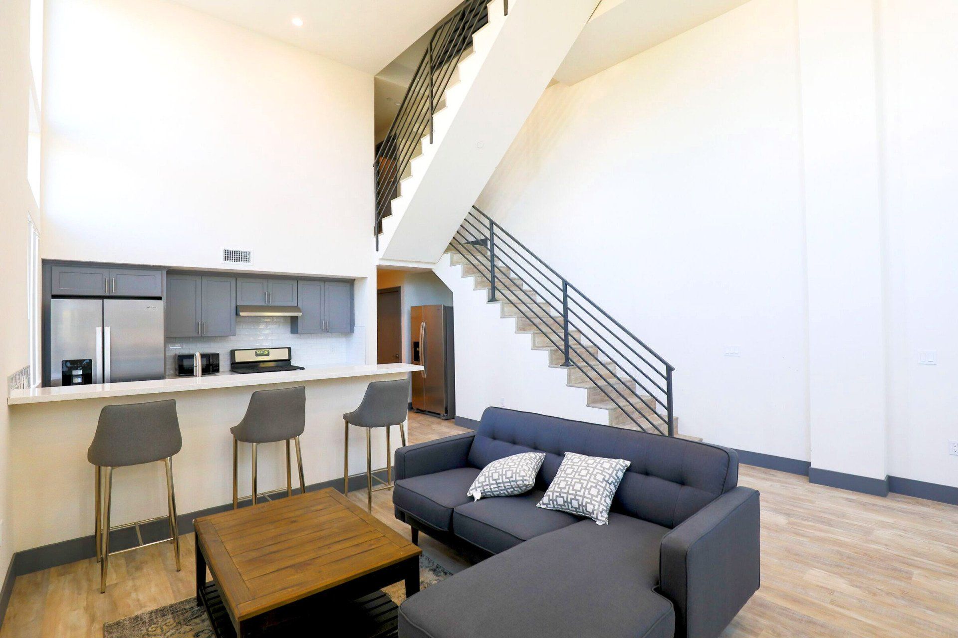 This image a showing a space where living room and kitchen are mixed together and stairs are starting from its right side.