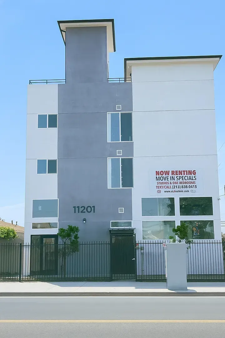 A modern three-story apartment building with gray and white exterior walls and the address 11201 near the front entrance.