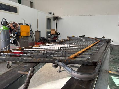 Officina industriale con una grande struttura metallica su supporti, cavi e attrezzi in un ambiente simile a un garage.