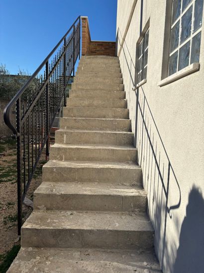 Scala esterna in cemento accanto a un edificio beige, con ringhiere in metallo nero e cielo azzurro sopra