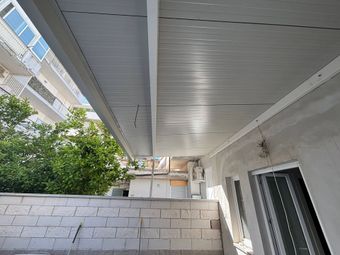 Corridoio esterno coperto accanto a palazzi residenziali, con un muretto basso e del verde sullo sfondo