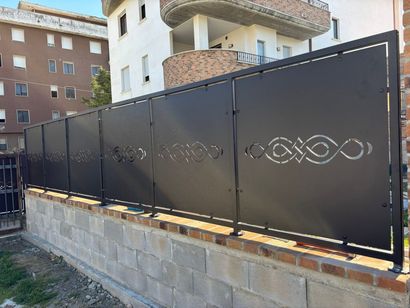 Recinzione in ferro nero con intagli decorativi lungo un muretto di pietra in una zona residenziale.