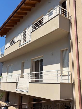 Esterno di un condominio con balconi beige e ringhiere bianche sotto un cielo azzurro